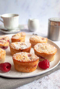 eight small raspberry and peach cakes on a white plate. A white teacup and saucer and a milk jug can be seen in the background.