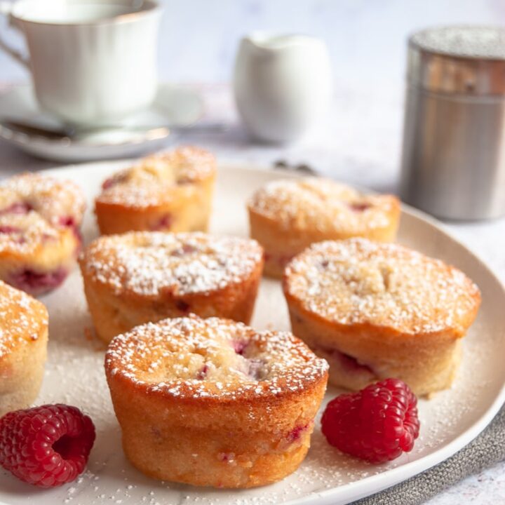 eight small raspberry and peach cakes on a white plate. A white teacup and saucer and a milk jug can be seen in the background.