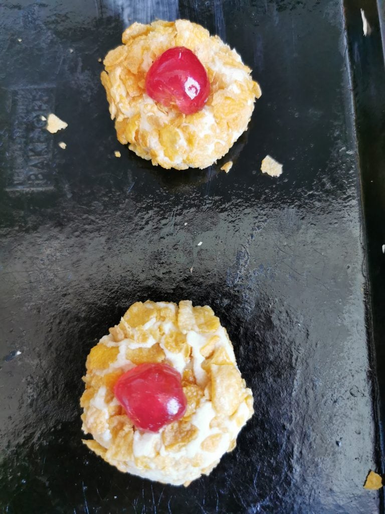 Unbakedcookies rolled in cornflakes and topped with a glace cherry.