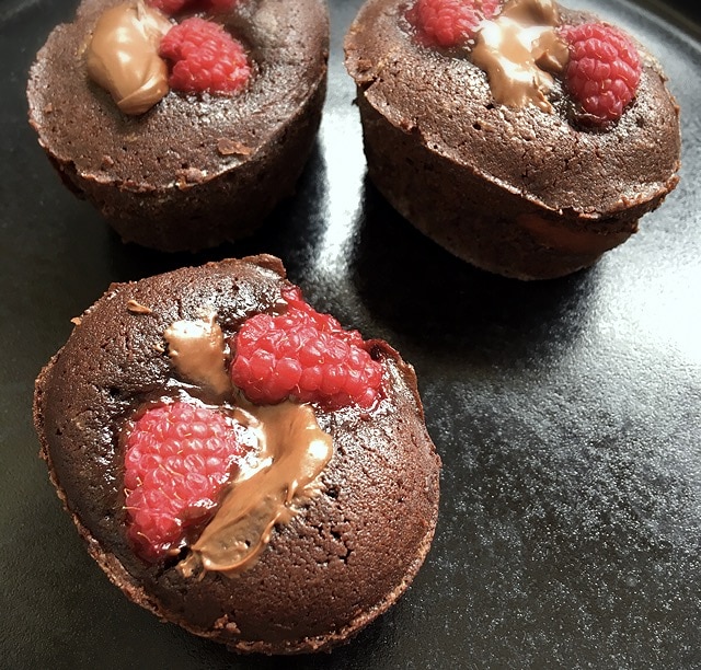 A close up picture of gooey chocolate cakes with raspberries and Nutella on a black plate.