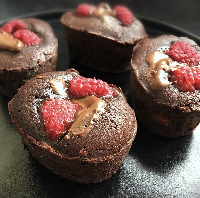 A close up photograph of gooey chocolate cakes with raspberries and Nutella on a black plate.