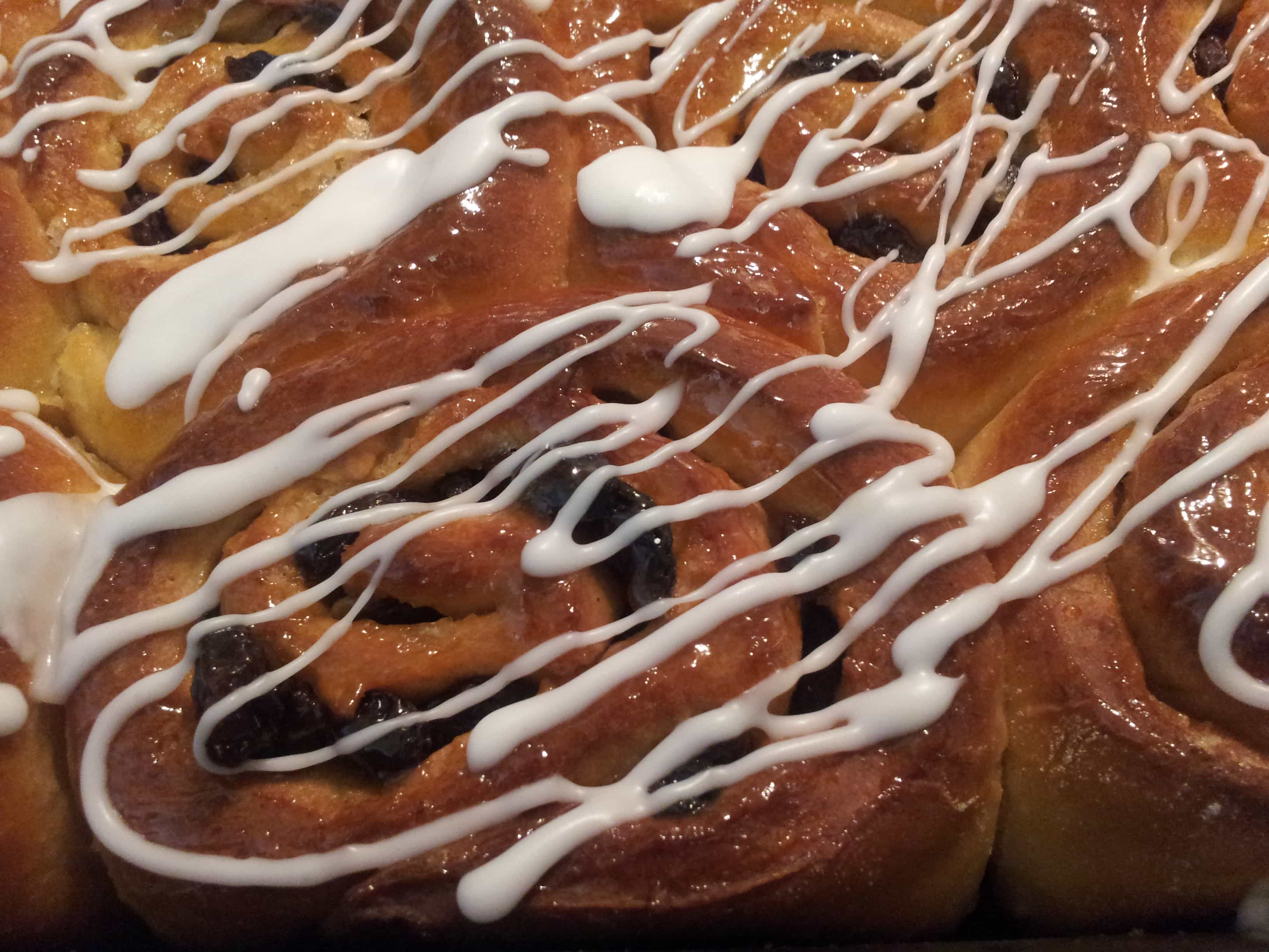 A close up photo of a batch of chelsea buns drizzled with white icing