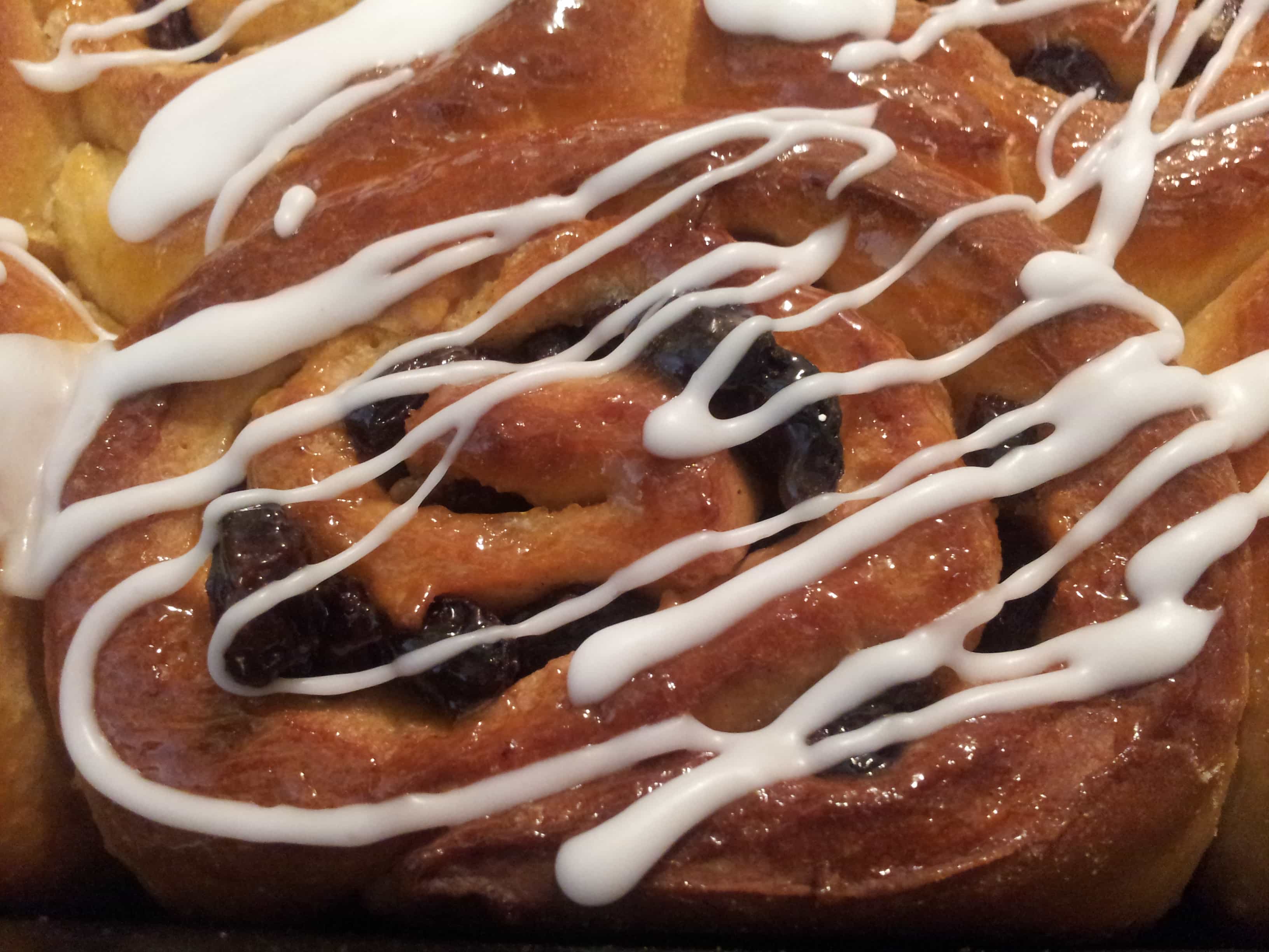 a close up photo of a sticky chelsea bun drizzled with white icing.