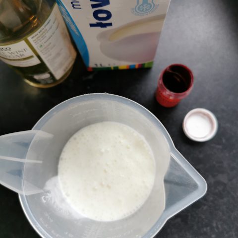 A jug of buttermilk, and bottle of vinegar and a small pot of red food colouring paste