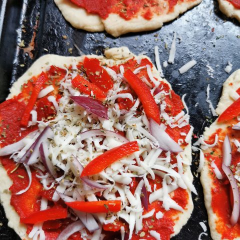 An uncooked pizza topped with cheese, onions and red peppers 