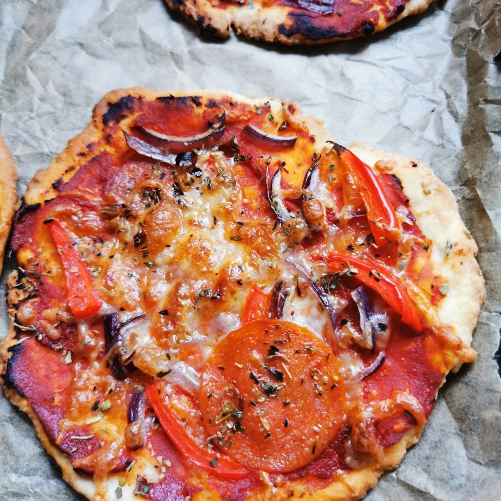 A mini pizza on a baking tray with tomato sauce, red onion and pepperoni