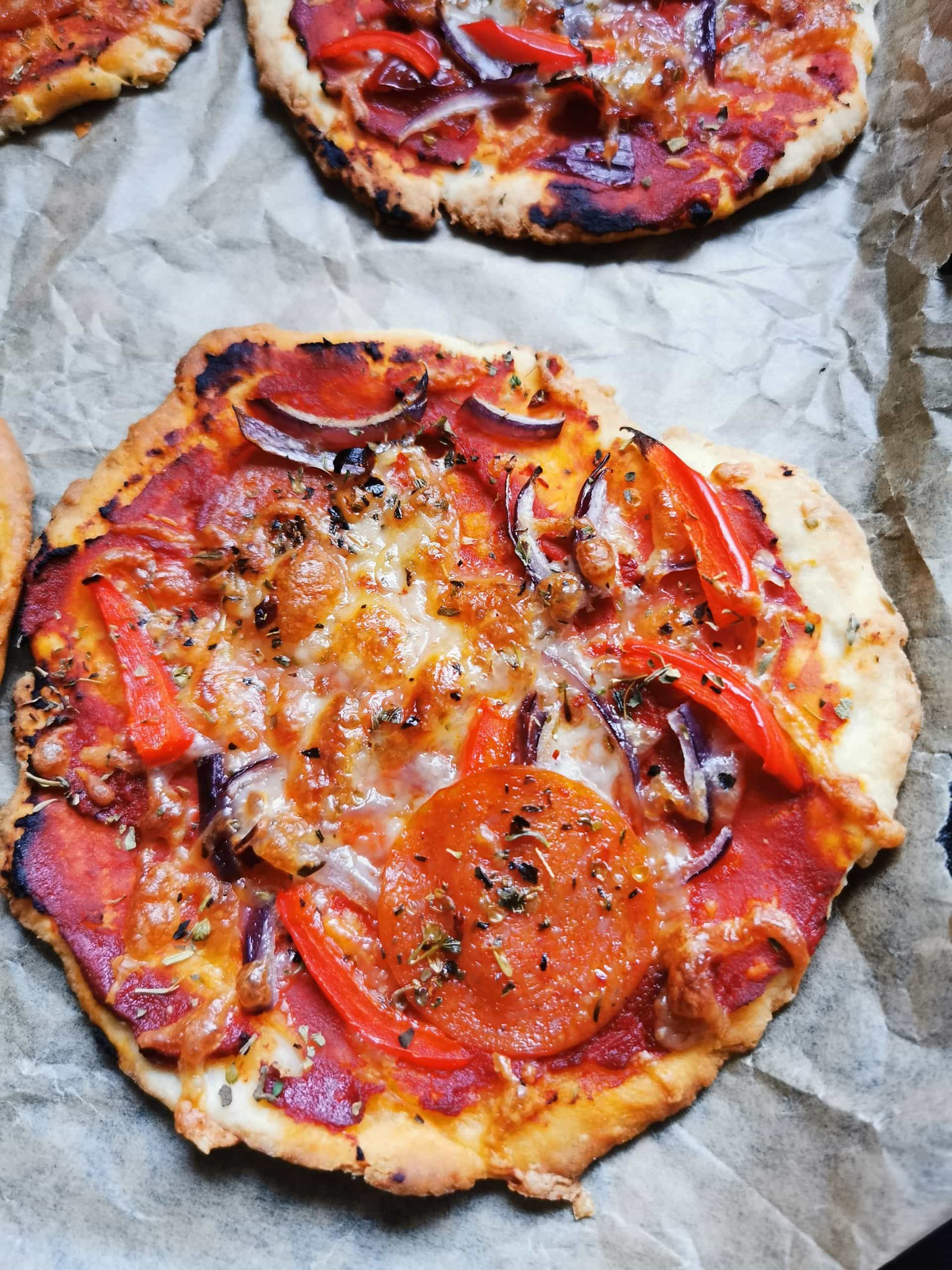 A mini pizza on a baking tray with tomato sauce, red onion and pepperoni 