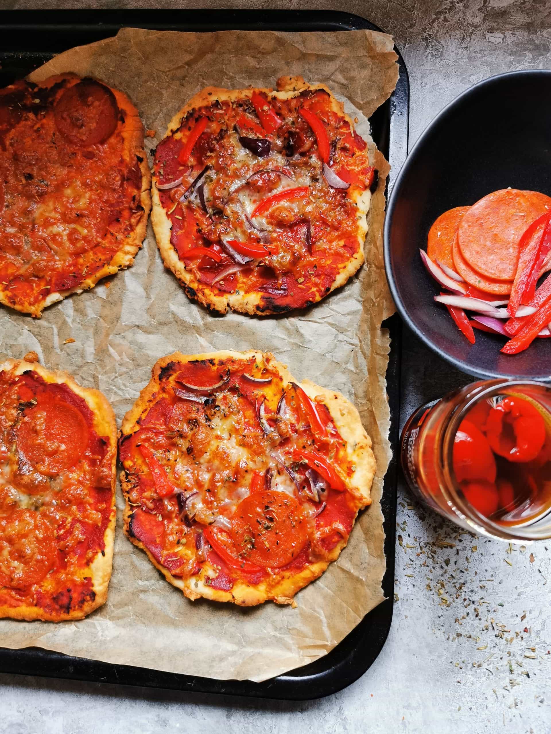 4 mini pizzas on a baking tray with tomato sauce, red onion and pepperoni