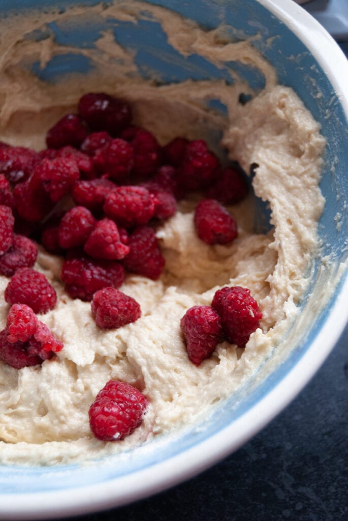 A blue and white mixing bowl filled with raspberry cake batter