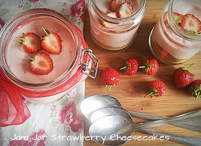 strawberry cheesecakes in jam fars topped with fresh strawberries on a wooden board with silver spoons