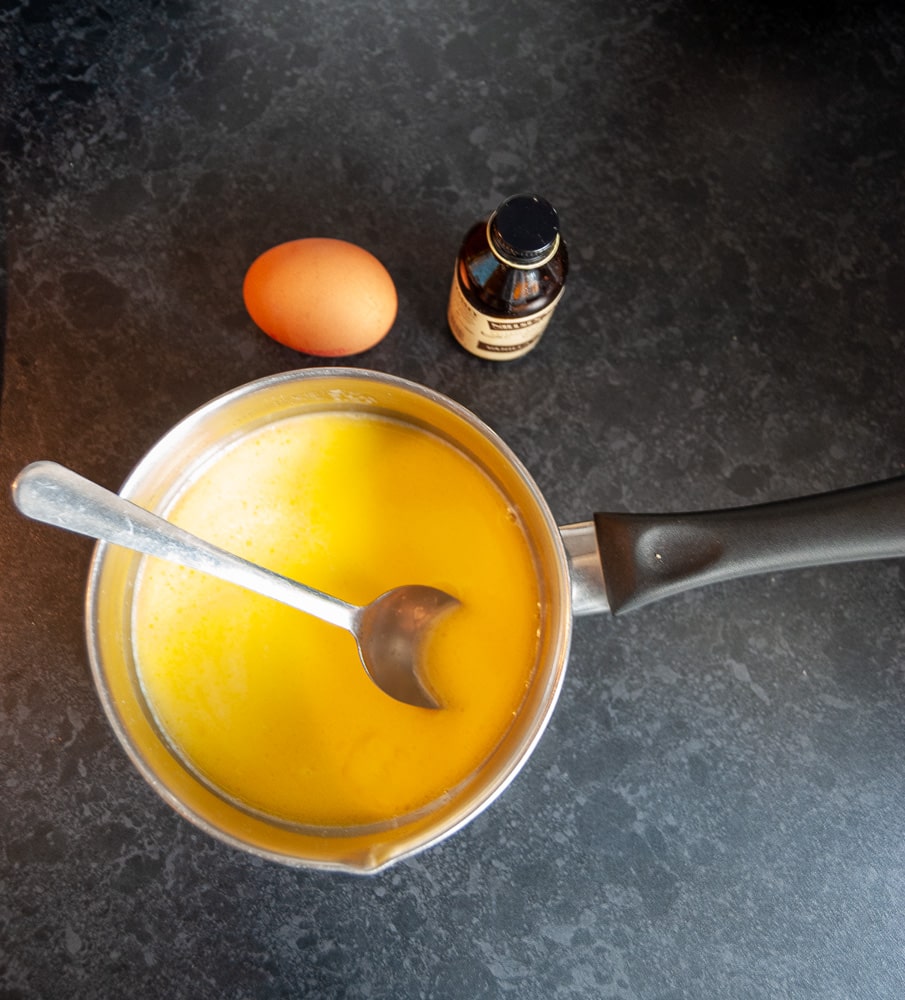 A pan of melted butter, an egg and a bottle of vanilla extract.