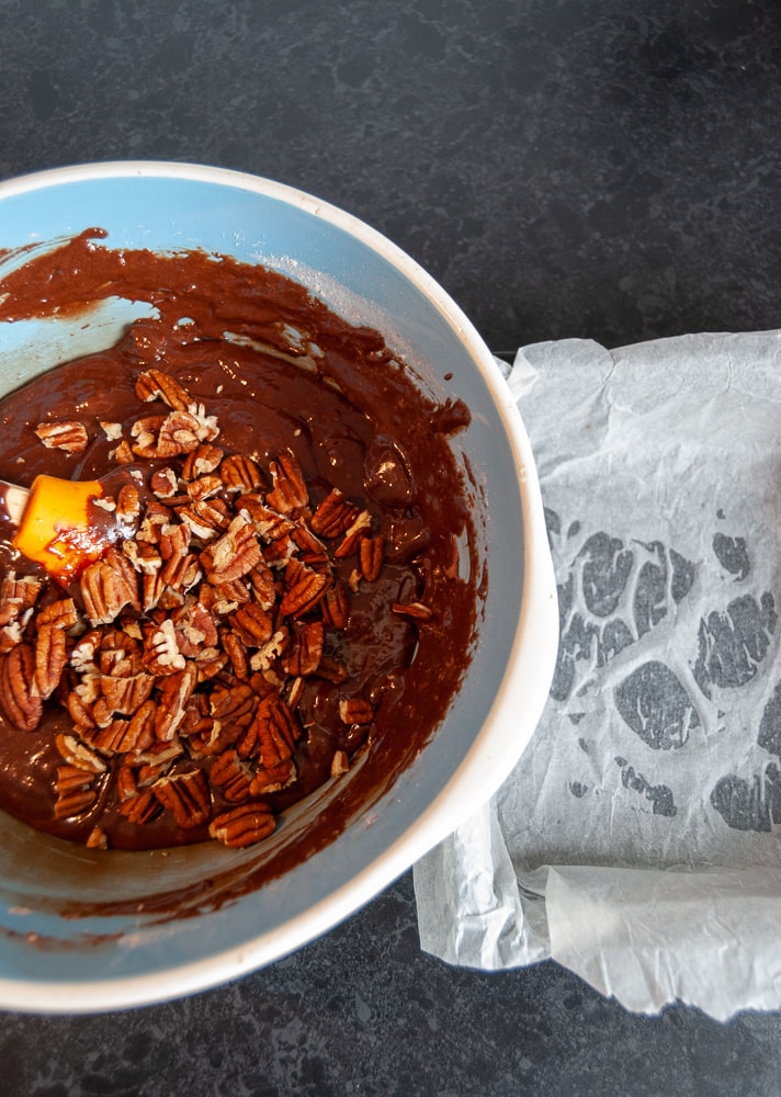 A bowl of brownie batter with chopped pecan nuts.