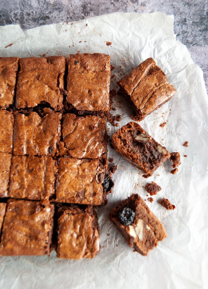 A flaylay photo of cherry and pecan brownies on a square of baking parchment.