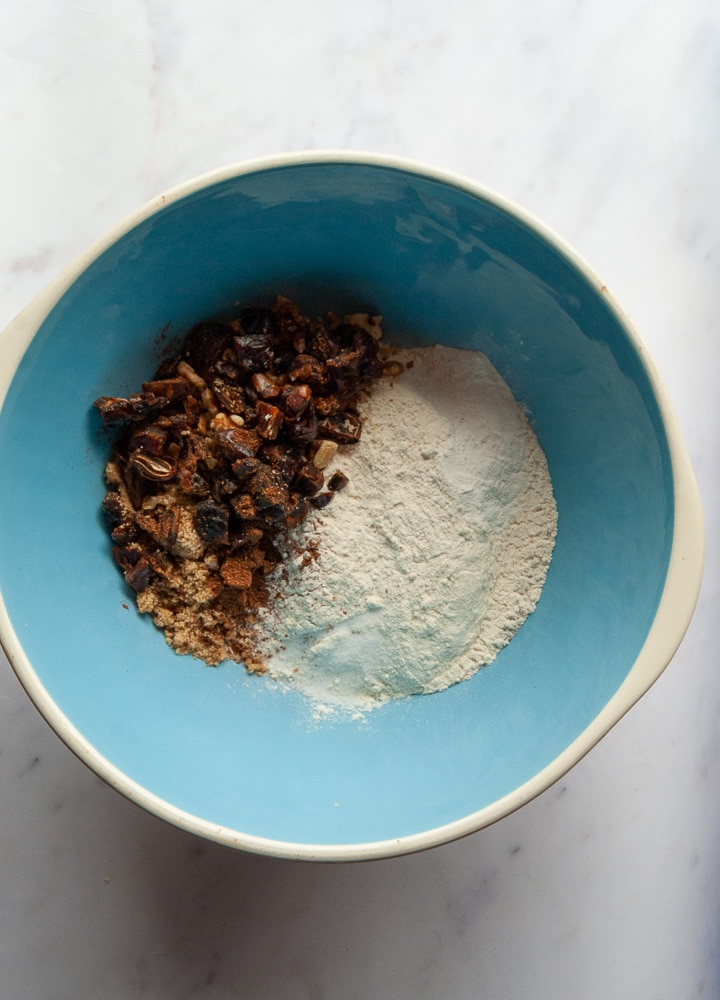 A blue and white bowl of flour, sugar, dates and walnuts for making scones.