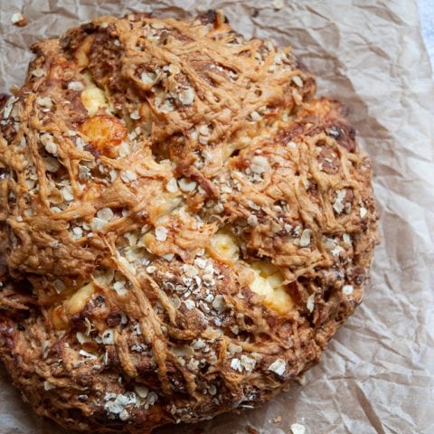 A freshly baked soda bread sprinkled with oats and cheddar cheese on a piece of baking parchment