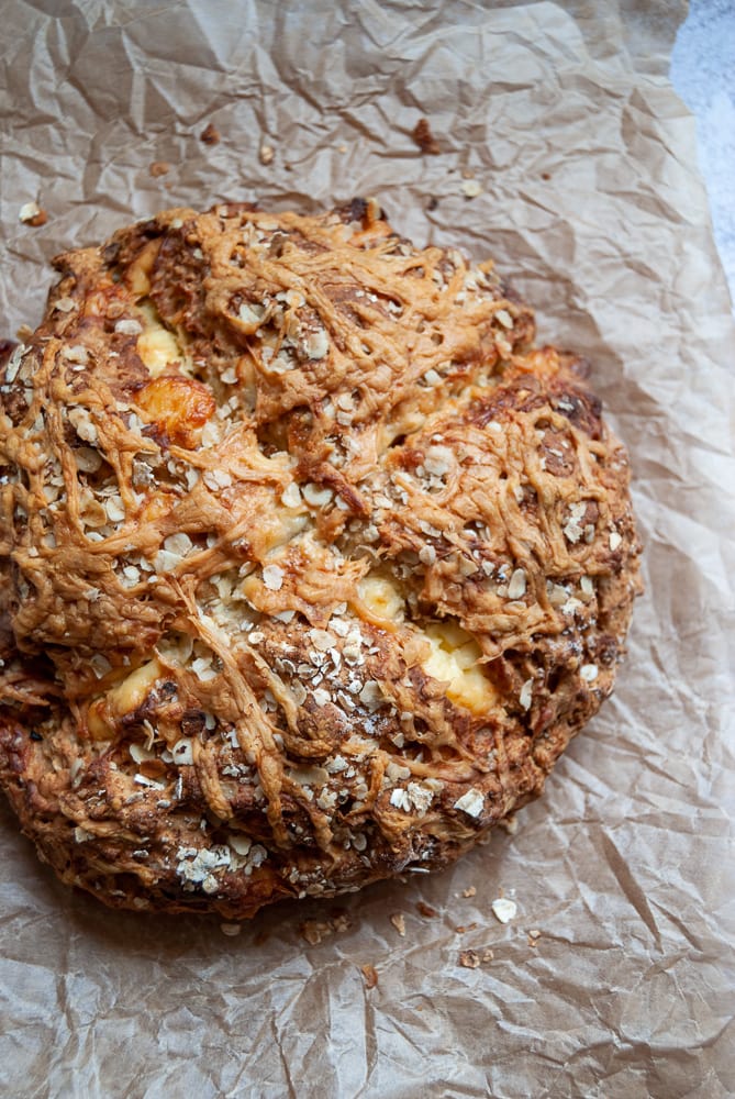 A freshly baked soda bread sprinkled with oats and cheddar cheese on a piece of baking parchment