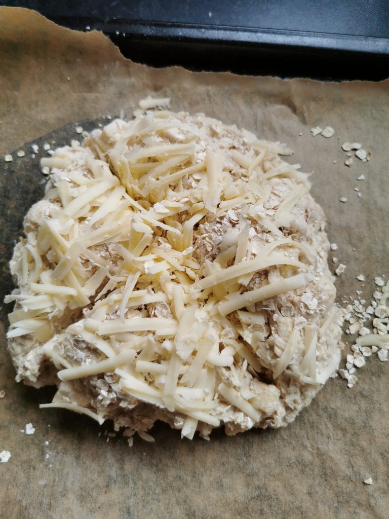 An unbaked soda bread sprinkled with cheese and oats