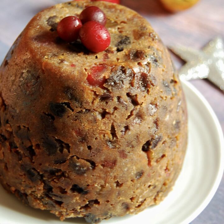 a christmas pudding topped with fresh cranberries on a white plate and a gold bauble and silver star in the background.