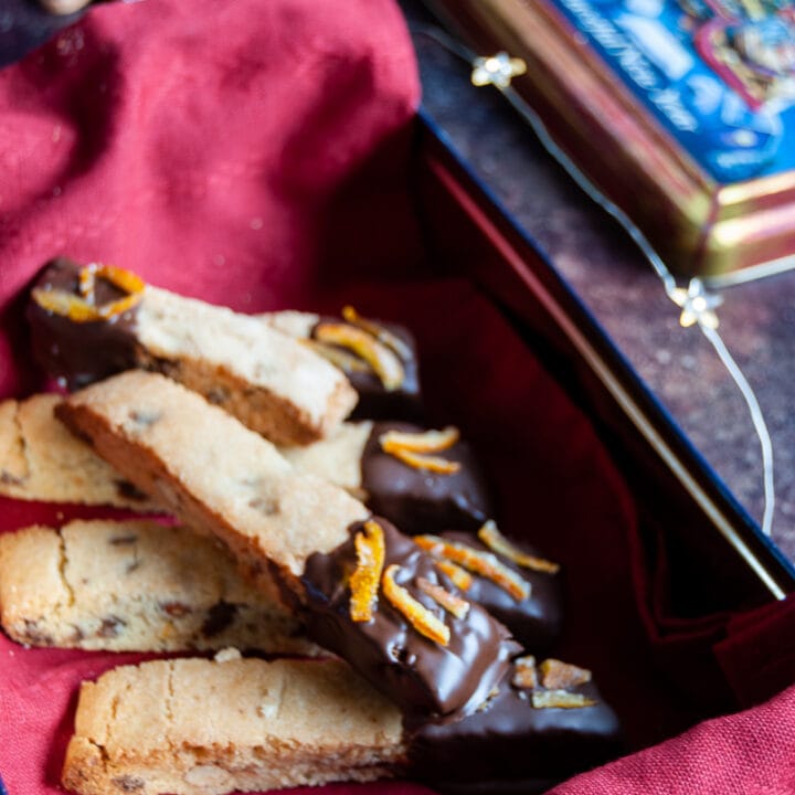 a box lined with a red napkin of biscotti cookies coated in chocolate and sprinkled with orange peel