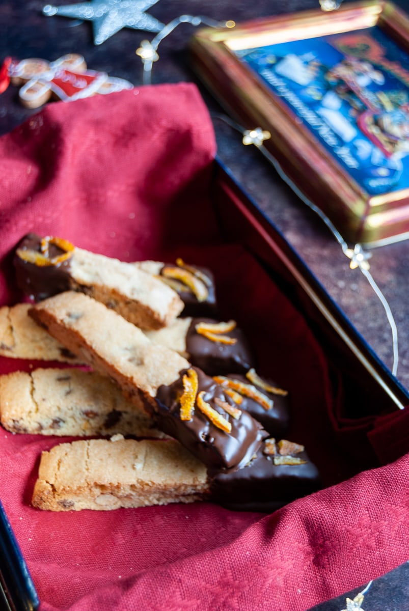 a box lined with a red napkin of biscotti cookies coated in chocolate and sprinkled with orange peel 