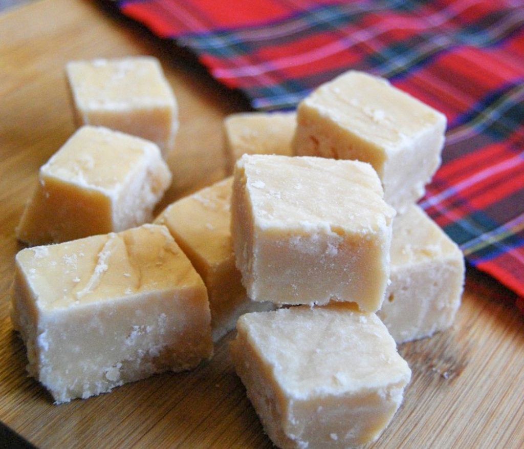 Pieces of Scottish tablet on a wooden board and a tartan blanket in the background. 