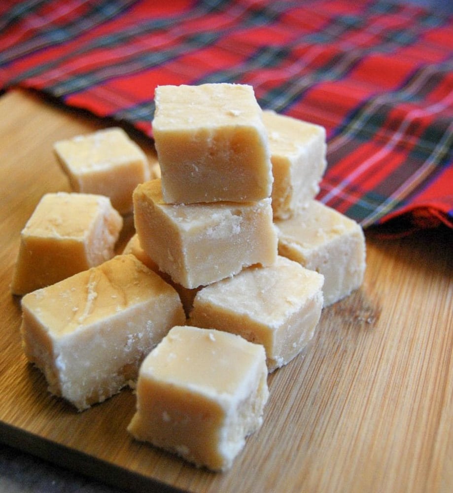Squares of Scottish Tablet sitting on a wooden board. A tartan tablecloth can be seen in the background.
