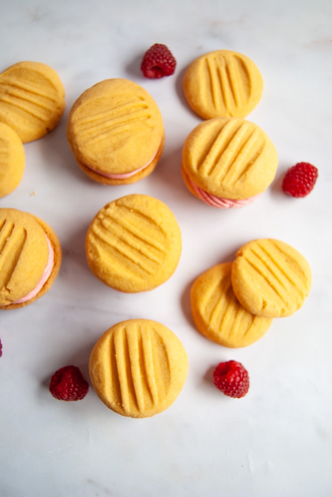 A flatlay photo of custard biscuits and fresh raspberries on a marbled white background.