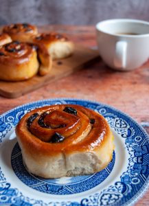 A Chelsea bun glazed with apricot jam on a blue and white Plate.