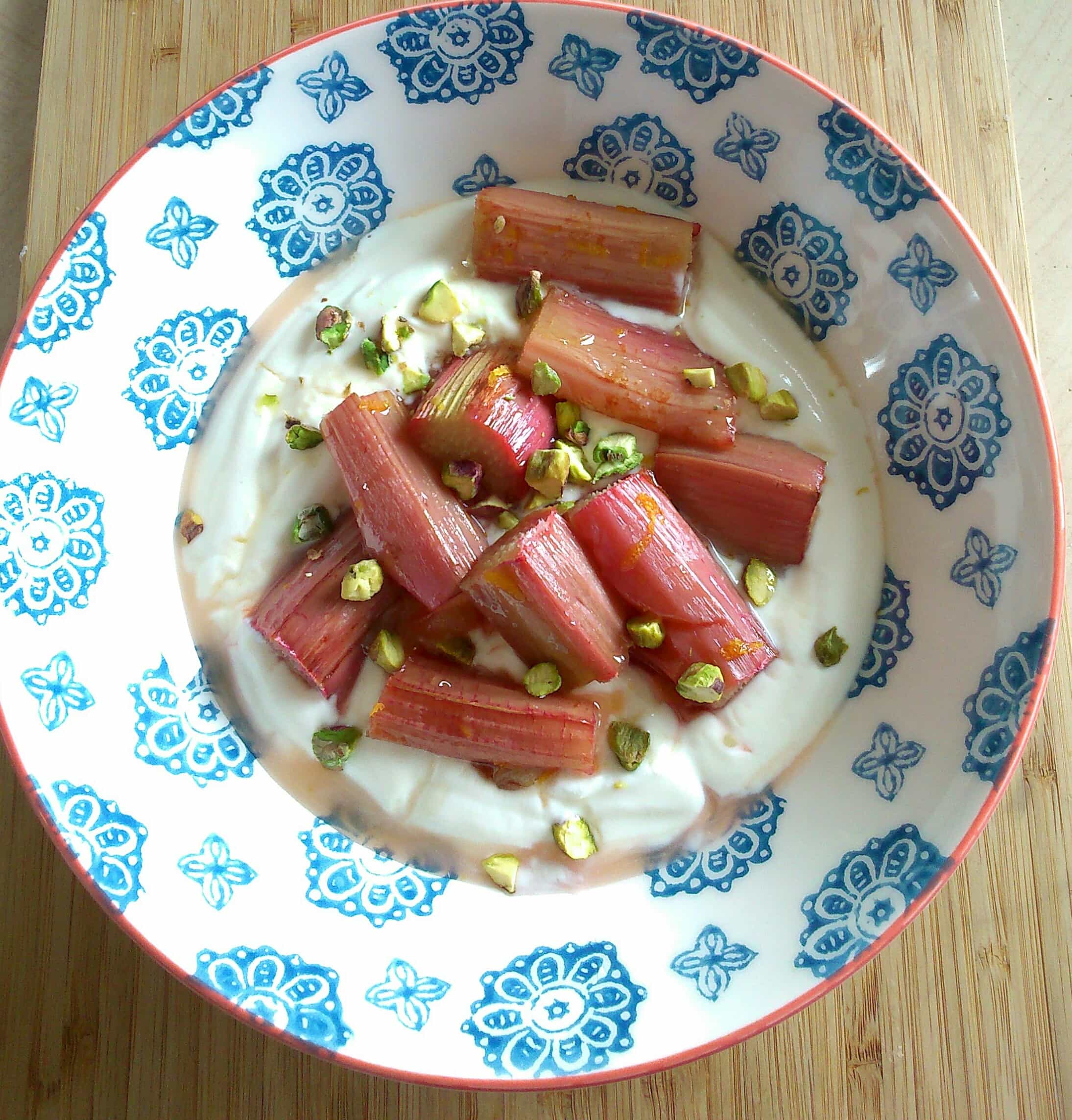 a blue patterned bowl with Greek yoghurt, roasted rhubarb and chopped pistachio nuts.