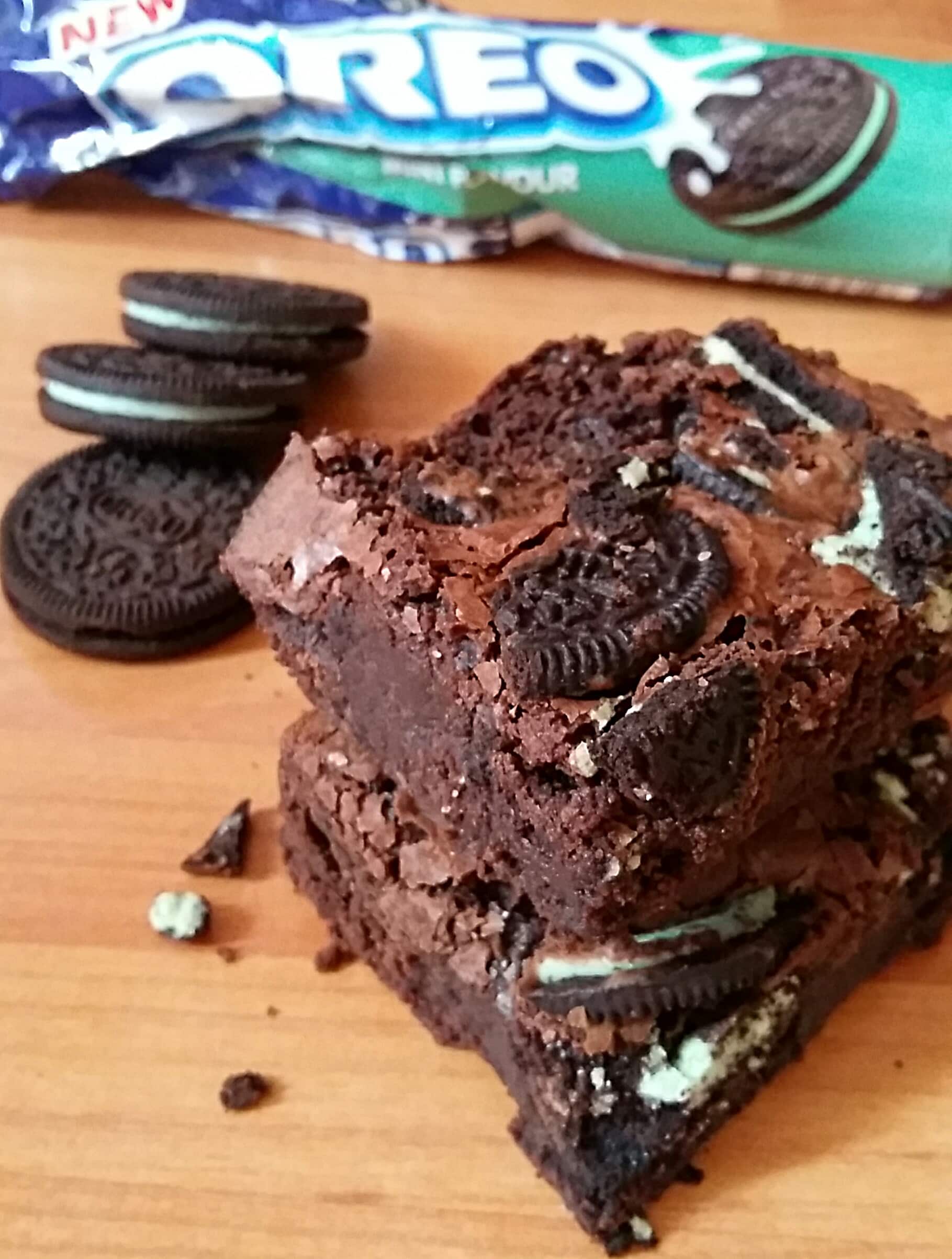 Three Mint Oreo Brownies sitting on top of each other. A packet of mint Oreo cookies can be seen in the background