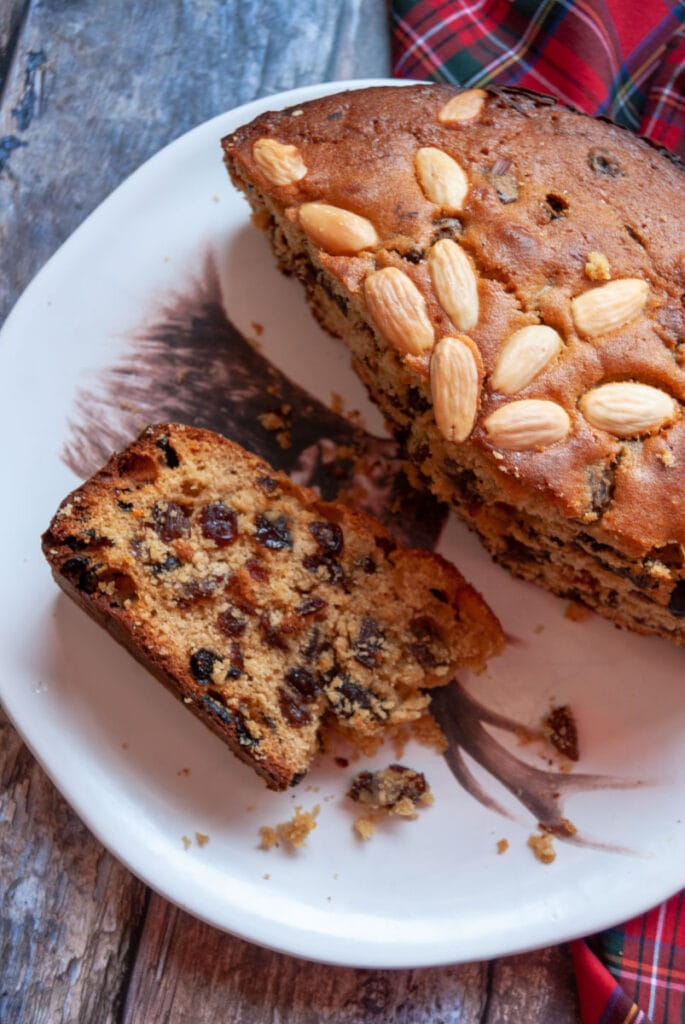 a fruit cake topped with blanched almonds on a white plate. 