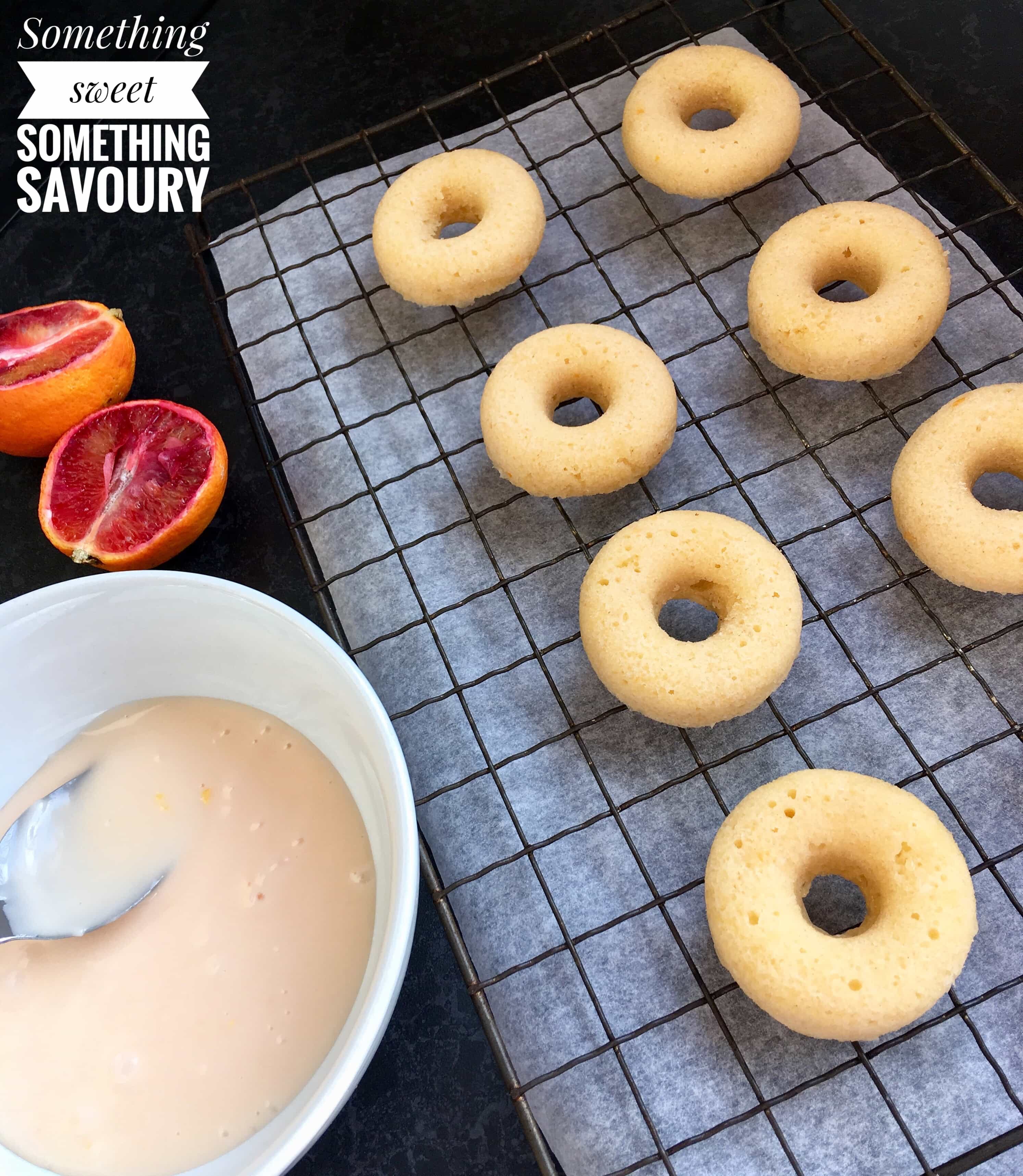 Freshly baked mini baked donuts on a wire rack with a bowl of orange icing ready to be drizzled over the donuts.