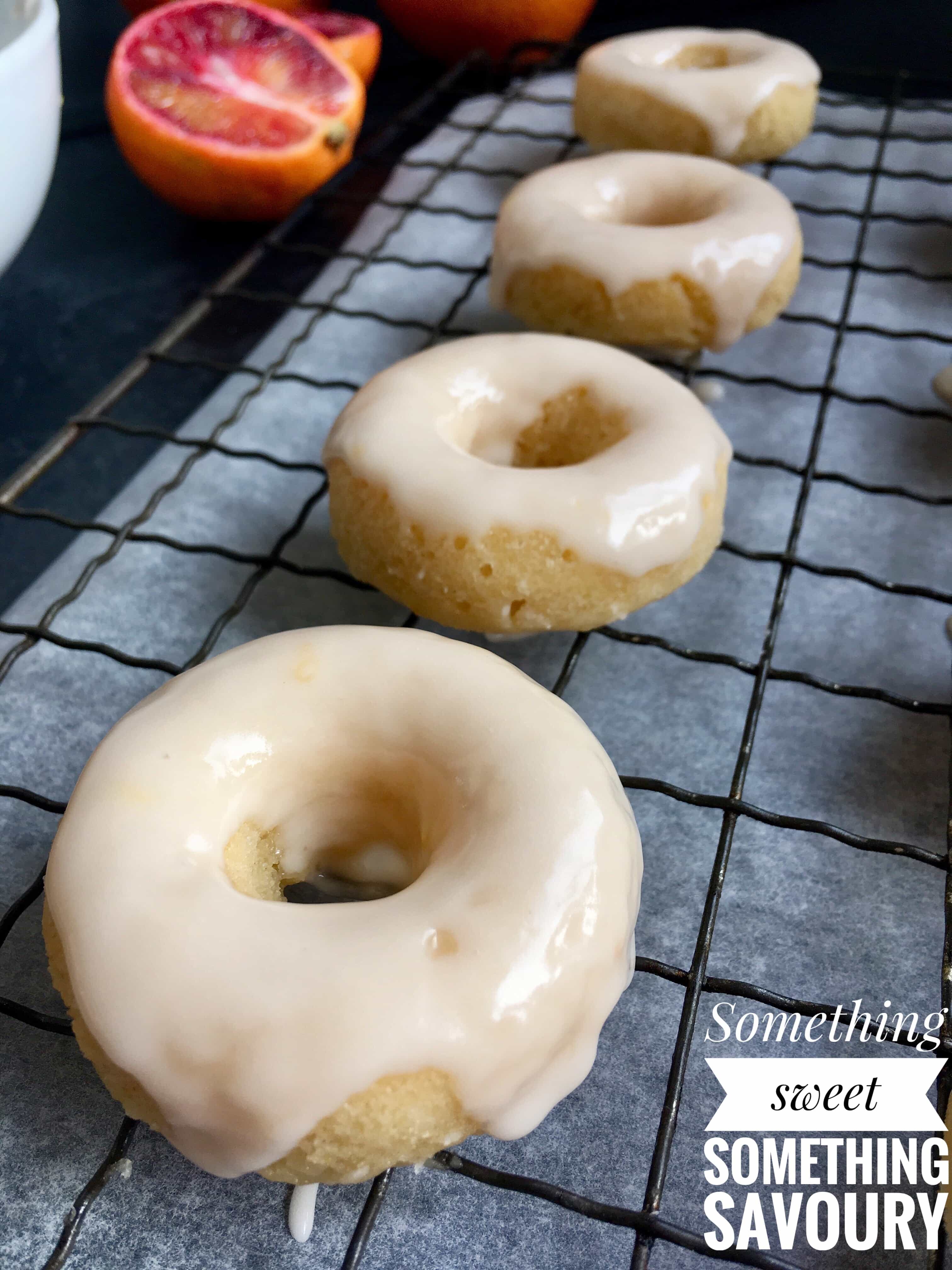 mini baked vanilla donuts covered in an orange glaze on a wire rack.