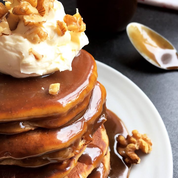 a pancake stack topped with whipped cream and chopped walnuts, covered in a rich toffee sauce.