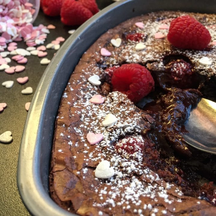 A spoon digging into a heart shaped chocolate brownie cake with raspberries