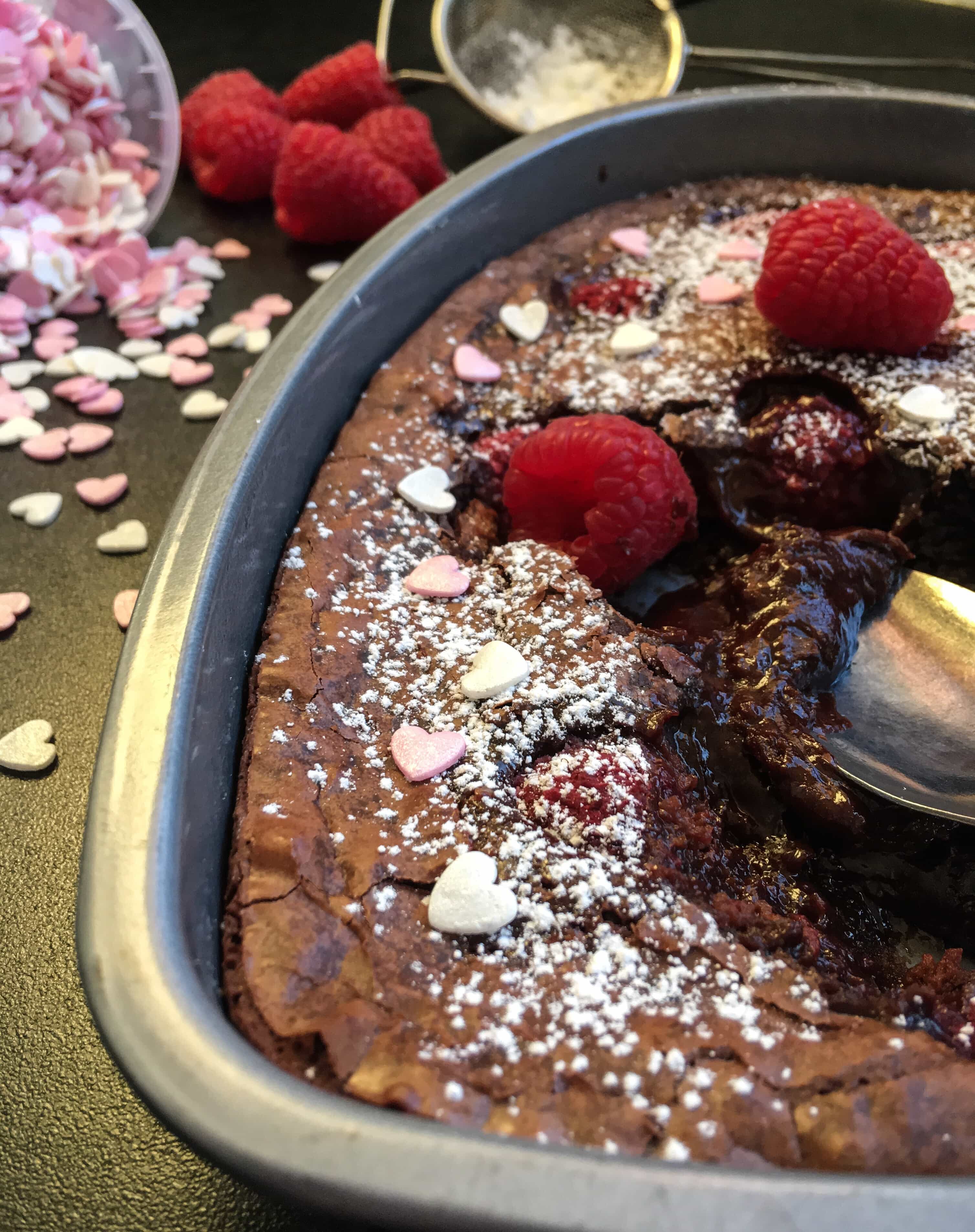 a picture of a heart shaped chocolate brownie cake with a spoon digging into the cake to reveal the molten chocolate centre.