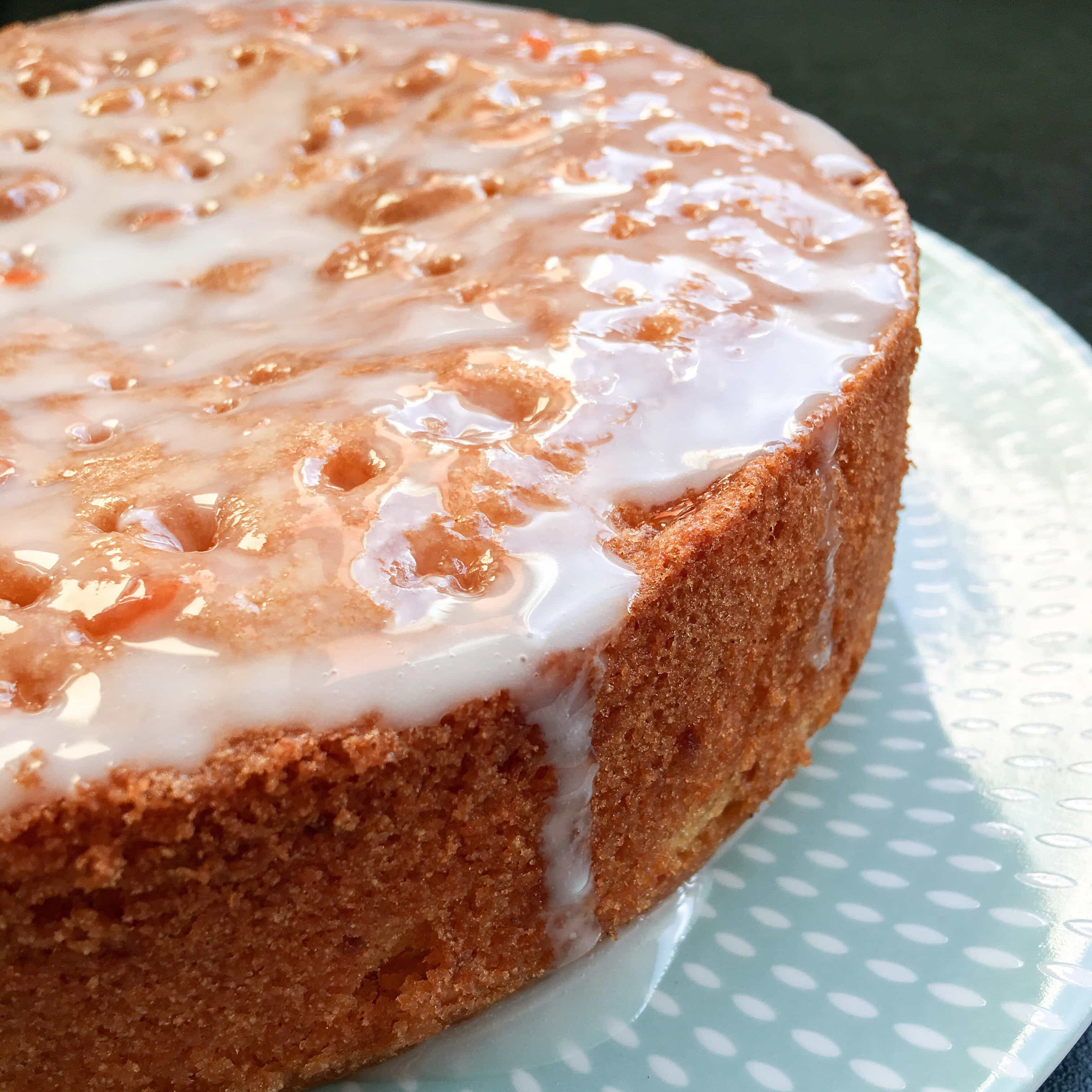 A round grapefruit cake with an icing drizzle on a green and white plate.