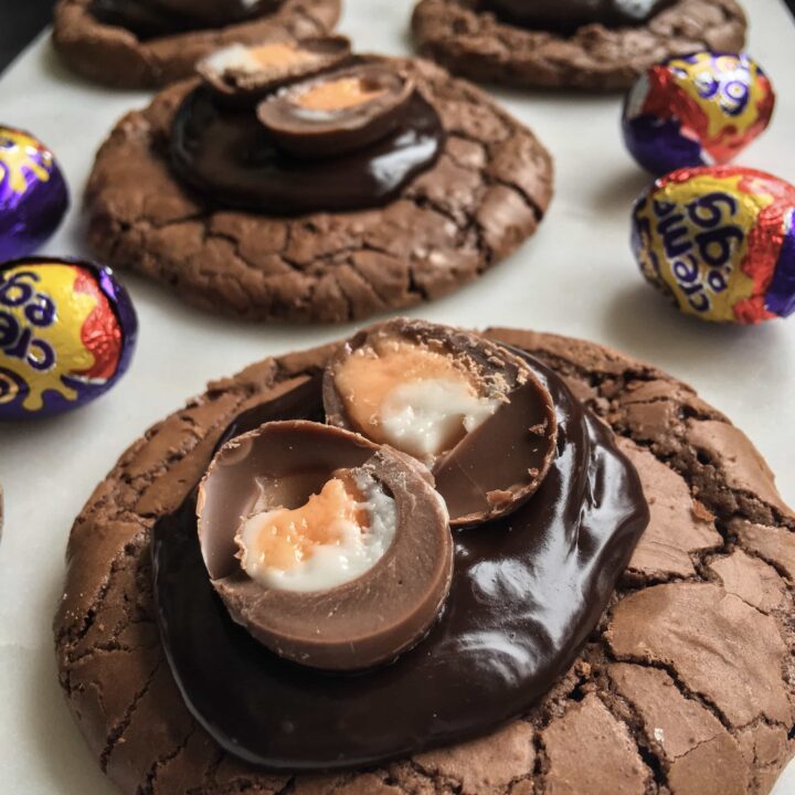 a close up picture of chocolate brownie cookies topped with chocolate ganache and a mini creme egg on a white board