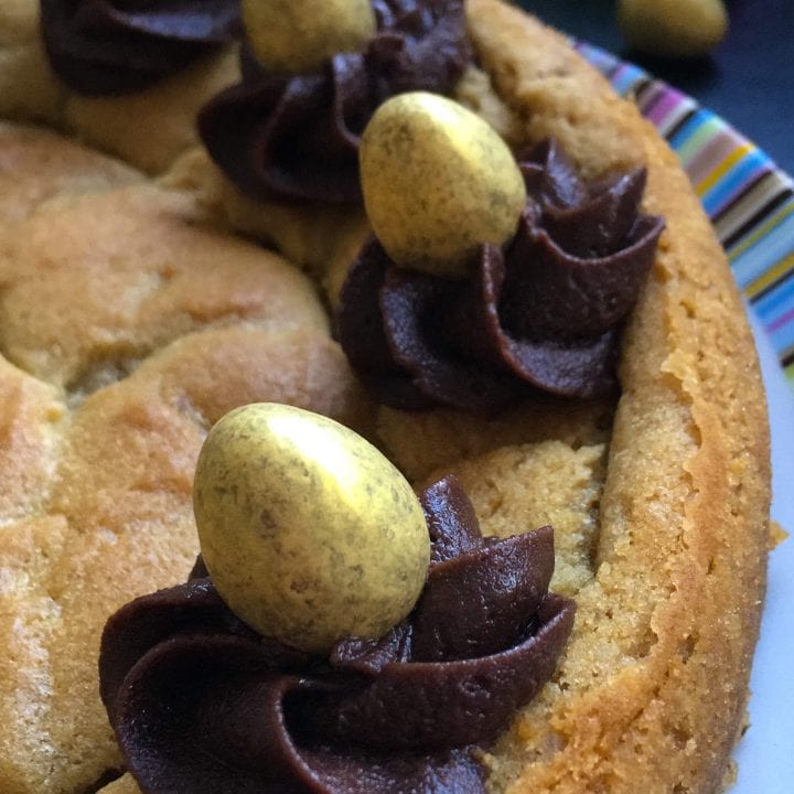 A close up picture of a giant chocoolate chunk cookie decorated with chocolate buttercream swirls and golden chocolate eggs