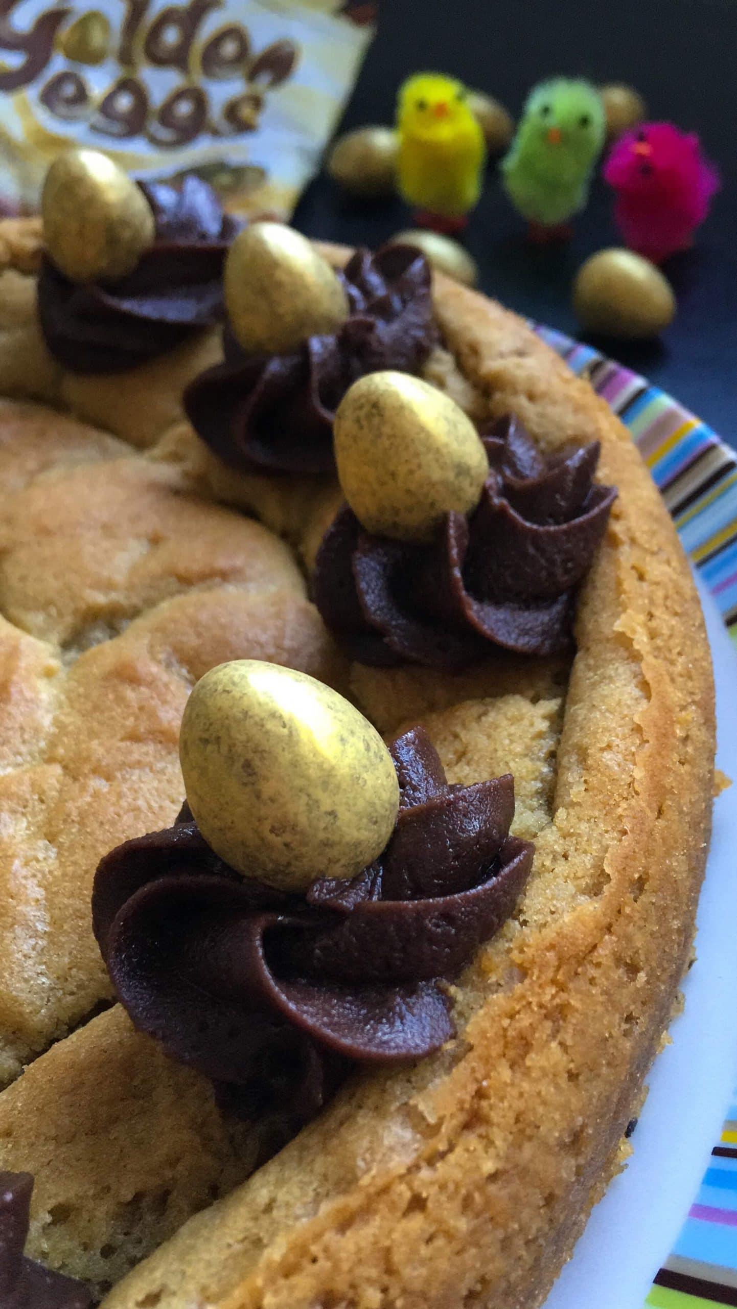 A close up picture of a giant chocoolate chunk cookie decorated with chocolate buttercream swirls and golden chocolate eggs