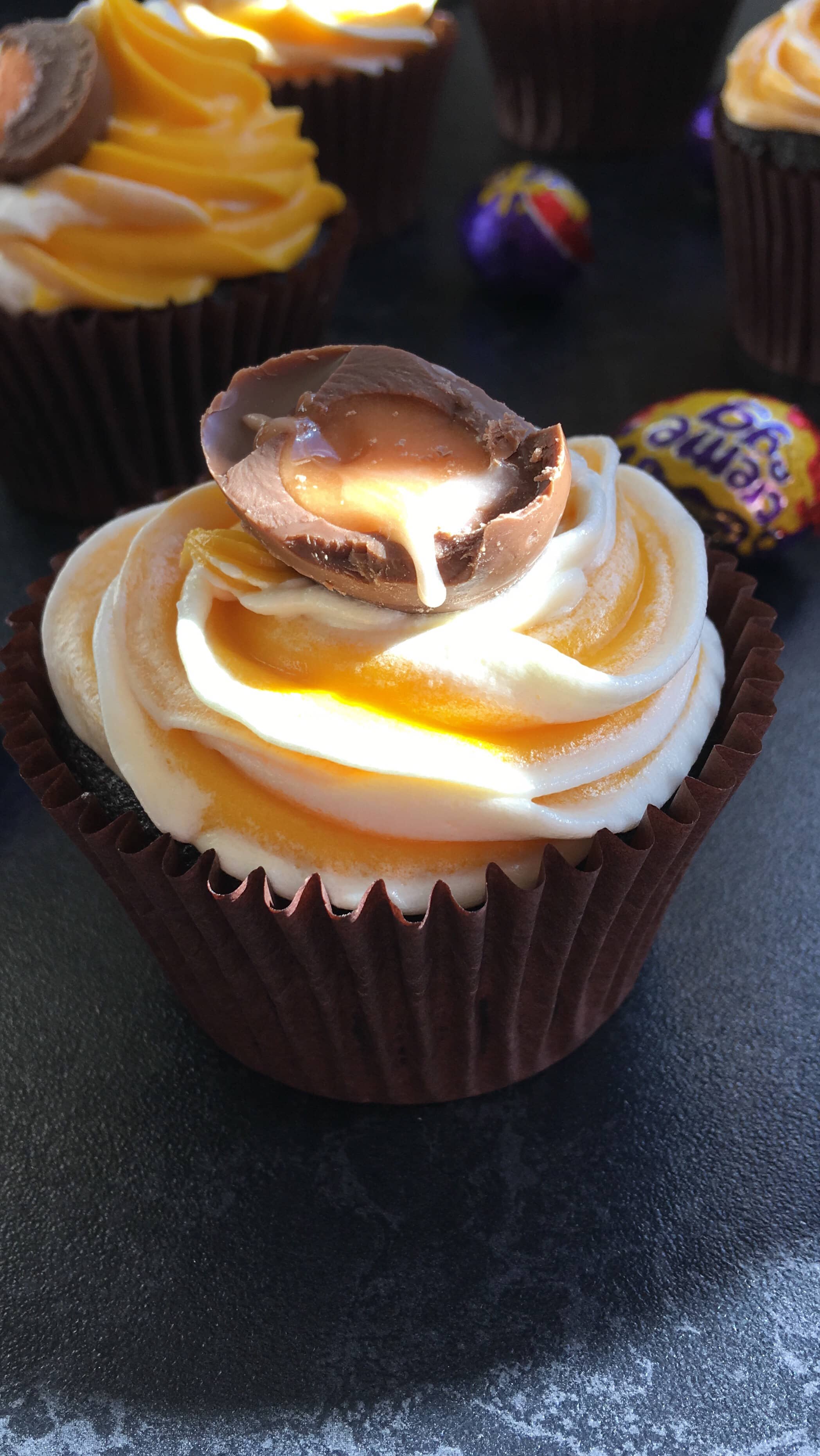 A chocolate cupcake topped with a white and yellow buttercream frosting and a creme egg cut open to reveal the filling.