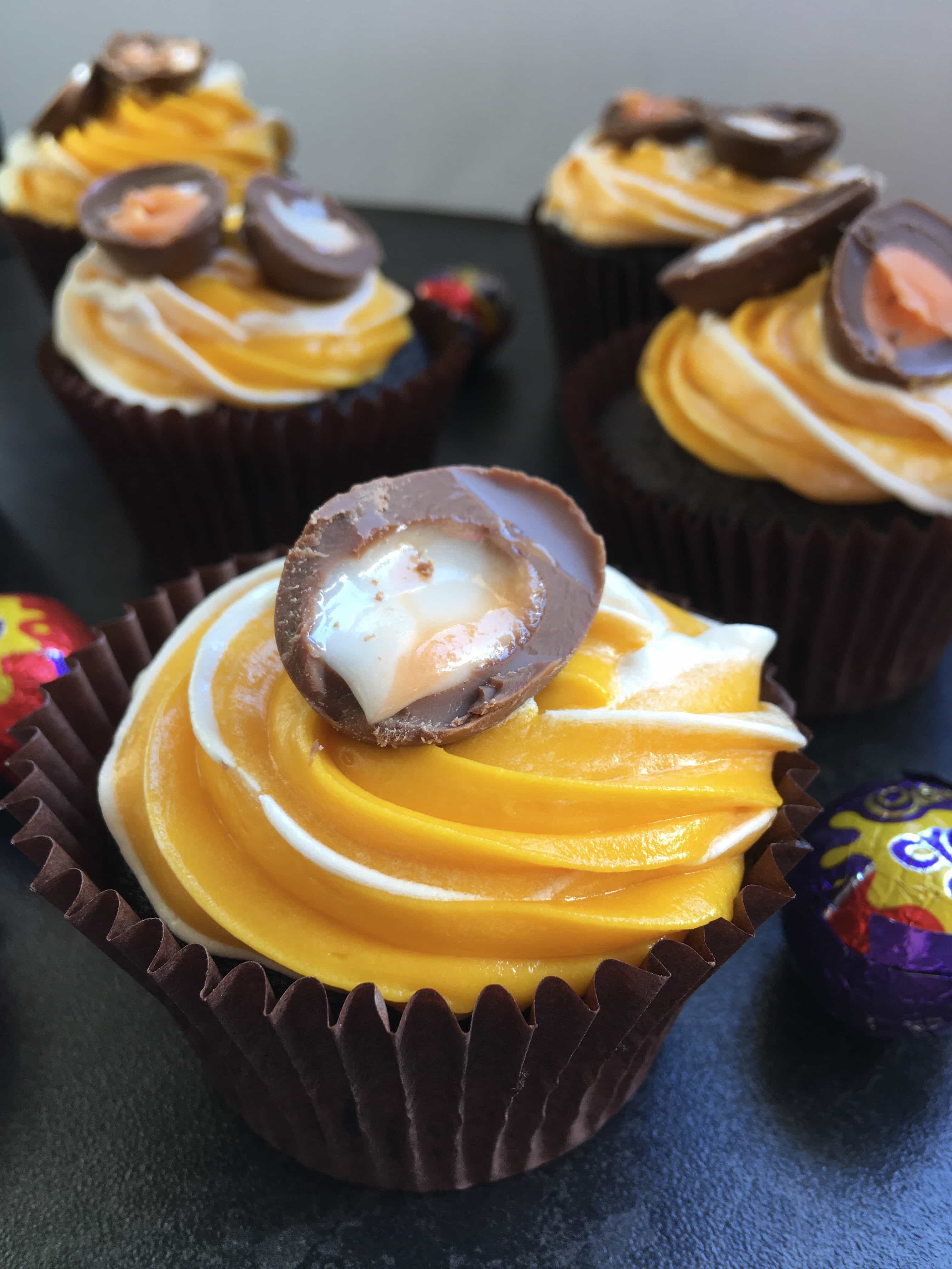 Chocolate cupcakes topped with yellow and white frosting and a mini creme egg