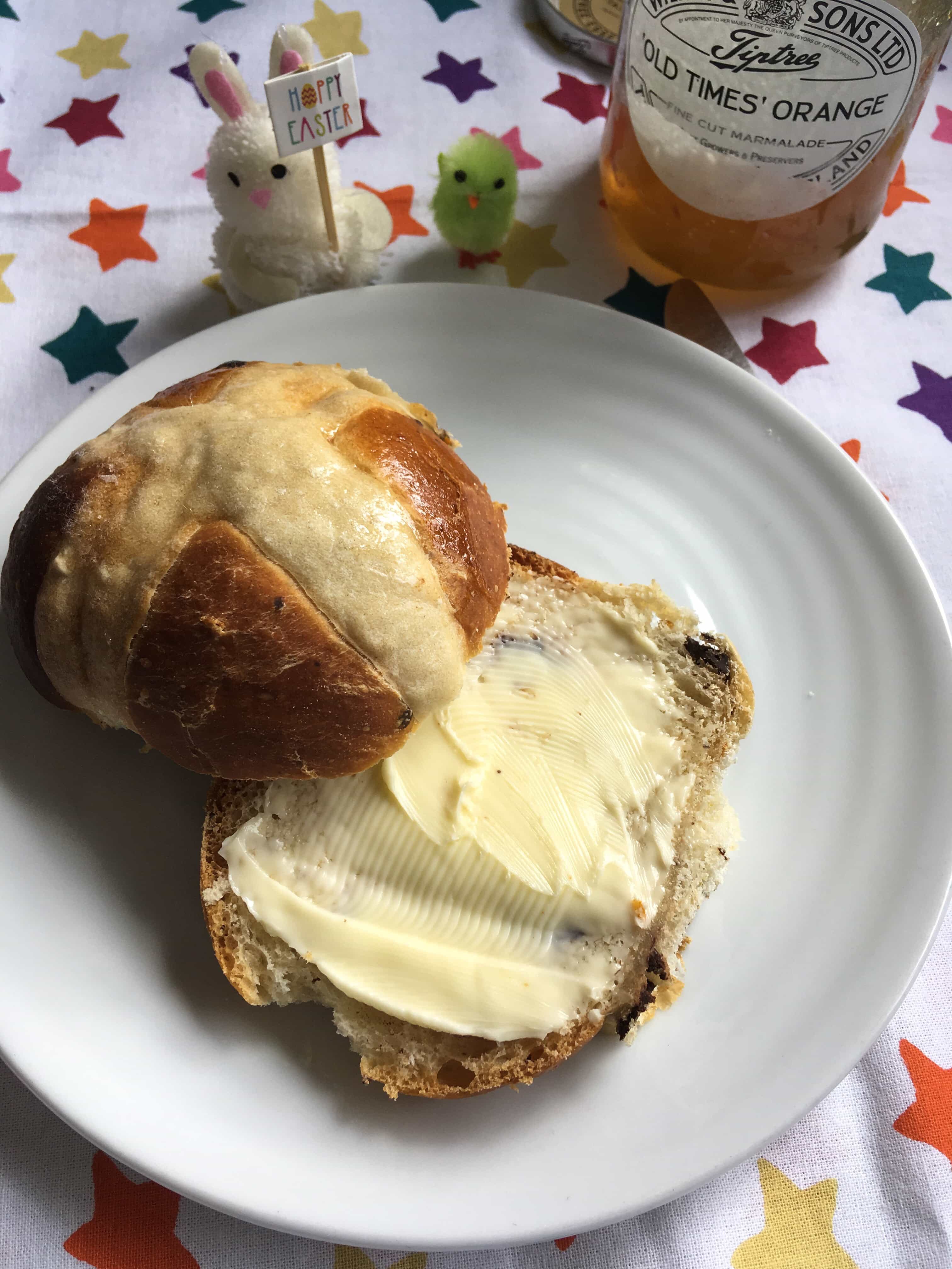 A chocolate orange hot cross bun split in half and spread with butter.