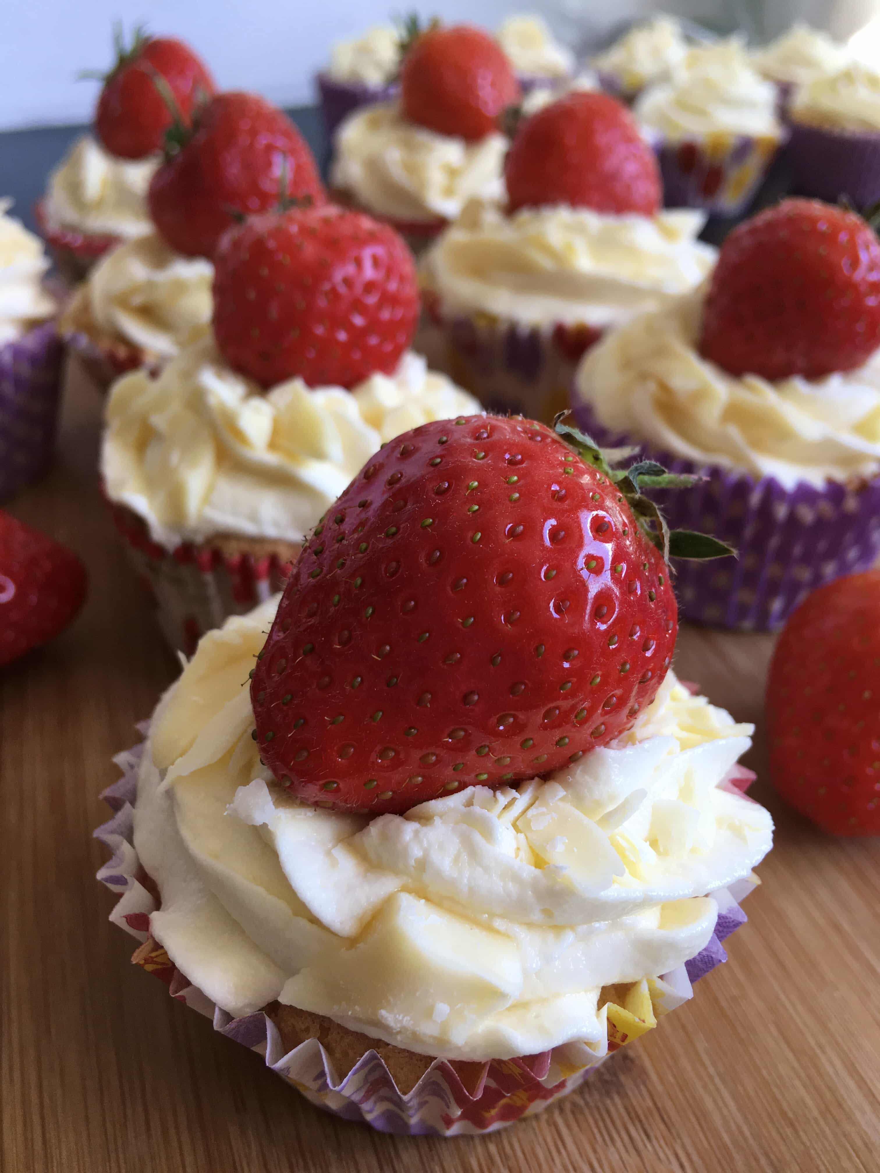 vanilla cupcakes topped with white chocolate buttercream frosting, a fresh strawberry and grated white chocolate.