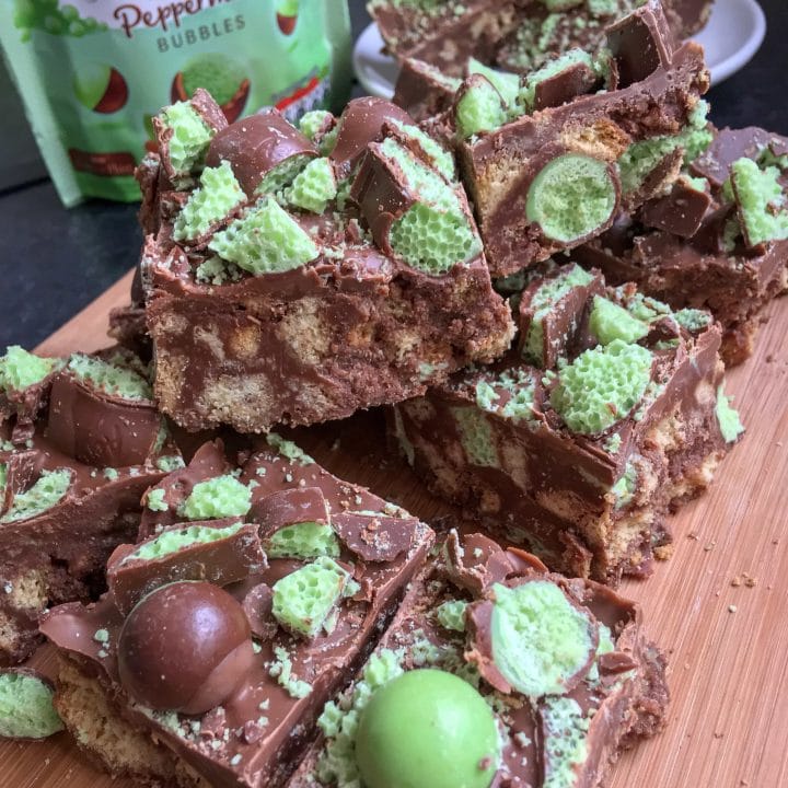 Squares of mint chocolate traybake topped with Aero chocolate on a wooden board