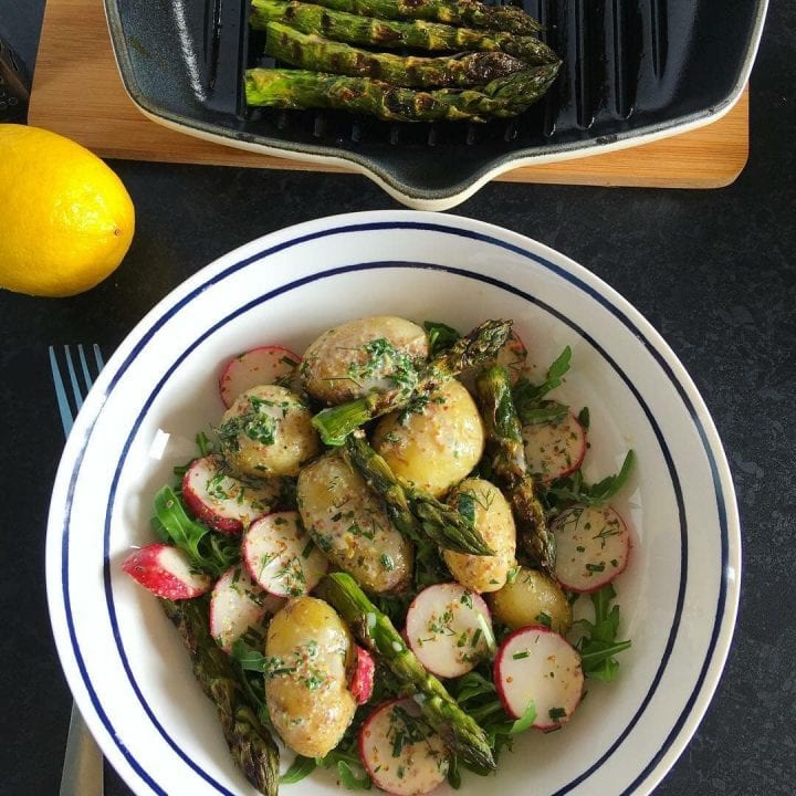 A bowl of new potatoes with griddled asparagus and radishes coated in a lemon buttermilk dressing. A griddle with chargrilled asparagus can be seen at the top of the picture.