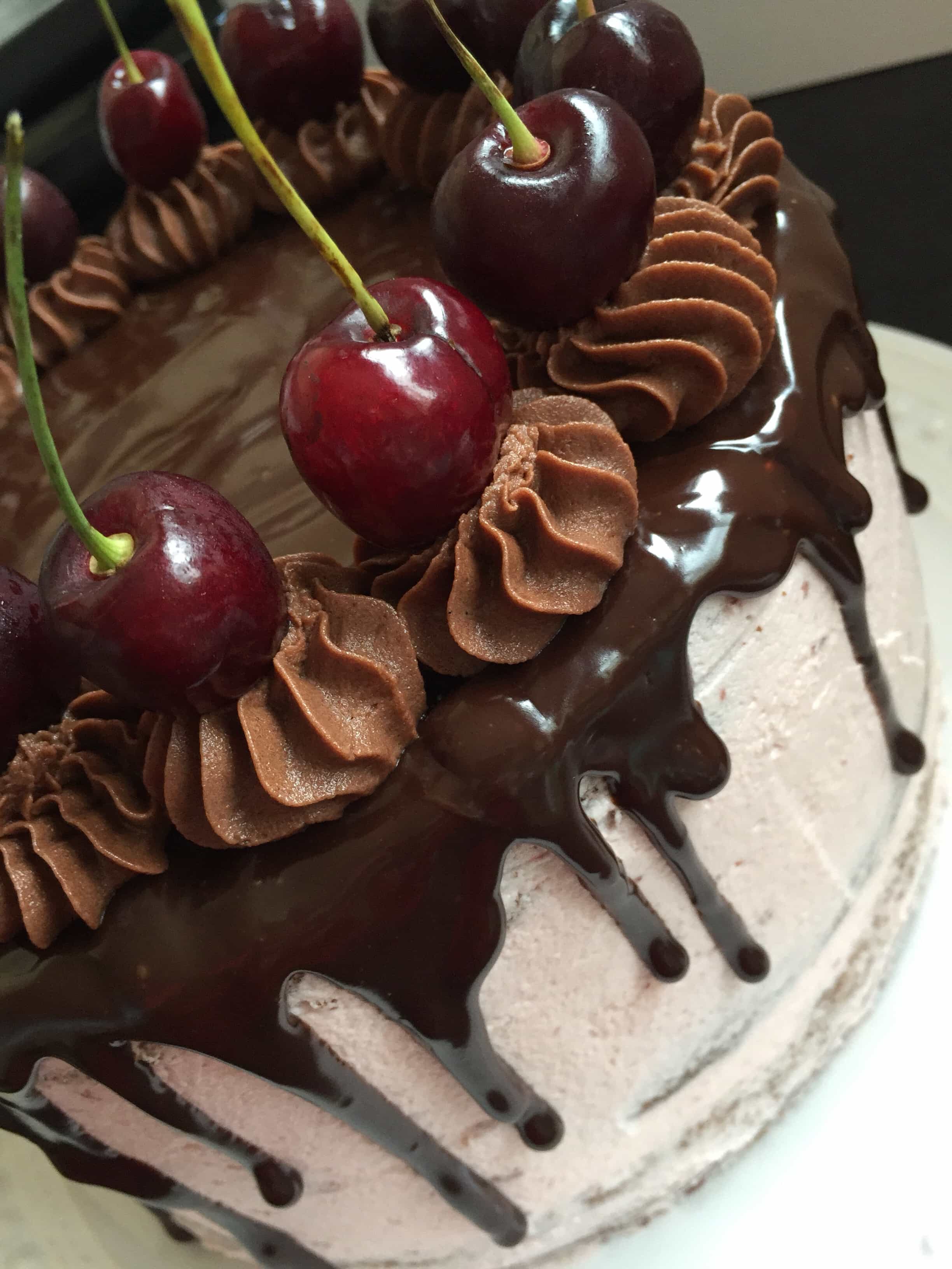 A close up picture of a chocolate cherry drip cake covered in a chocolate ganache drip and topped with fresh cherries