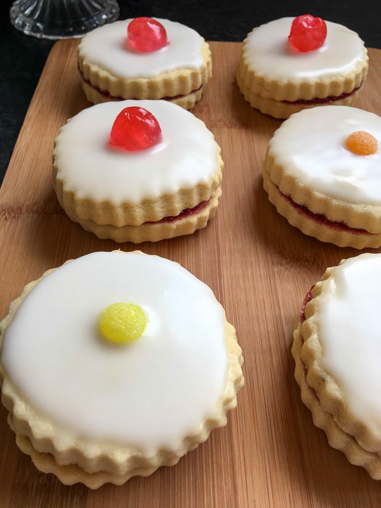 Six empire biscuits topped with white icing and cherries/coloured jelly sweets.