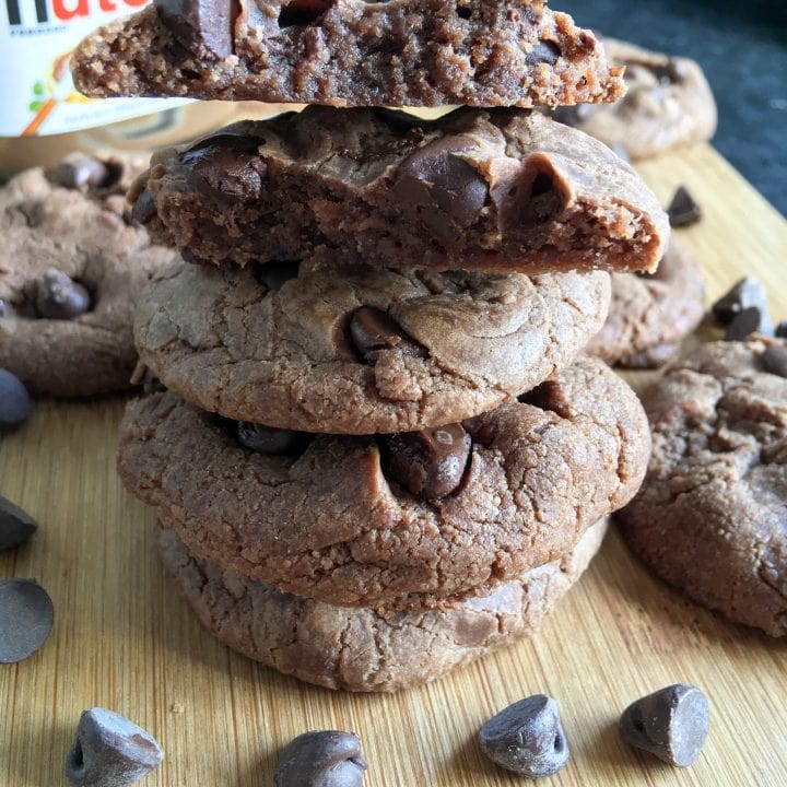 A stack of Nutella cookies with chocolate chip. A jar of Nutella and more cookies can be seen in the background.