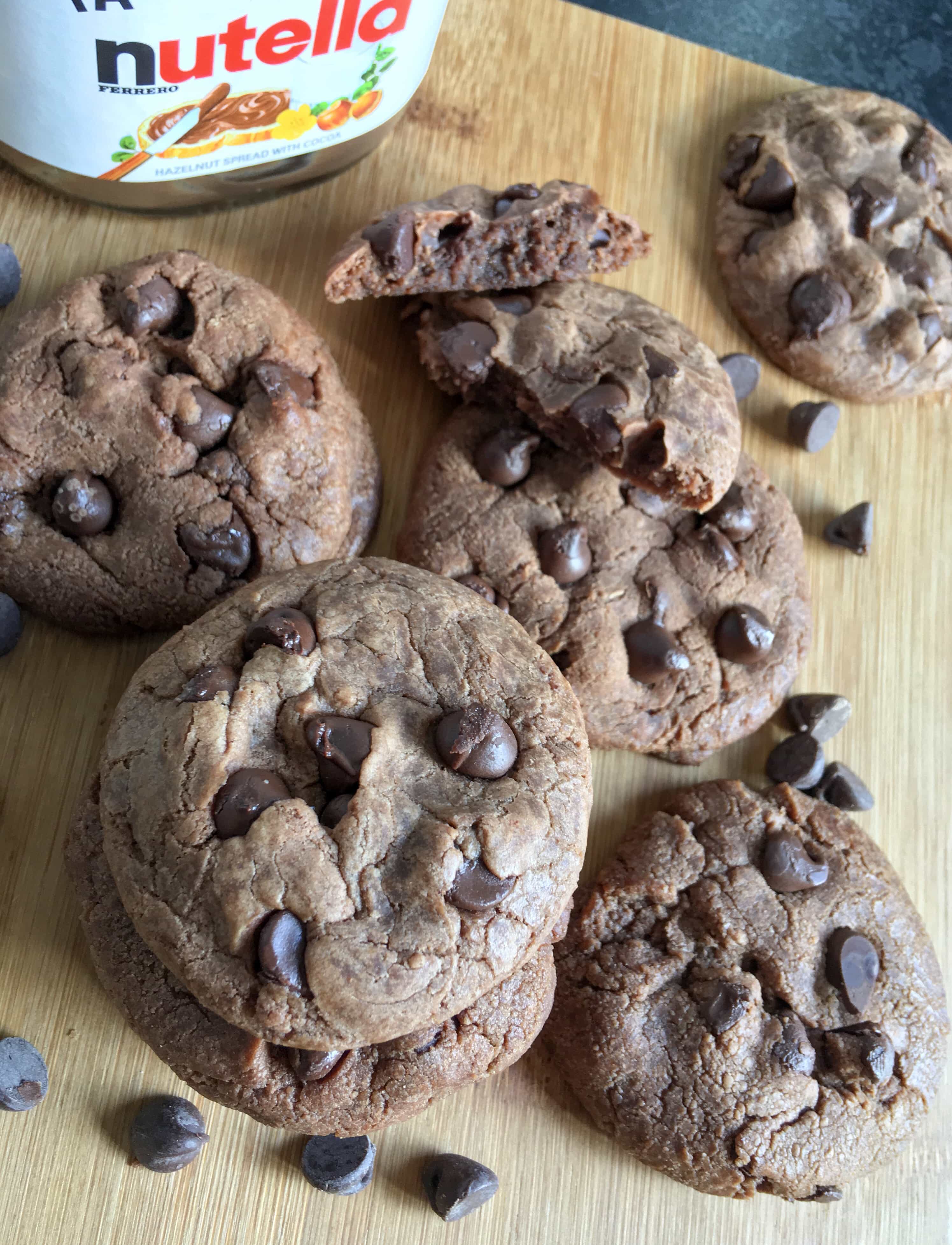 A flat lay photo of Nutella cookies with  with chocolate chips on a wooden board.